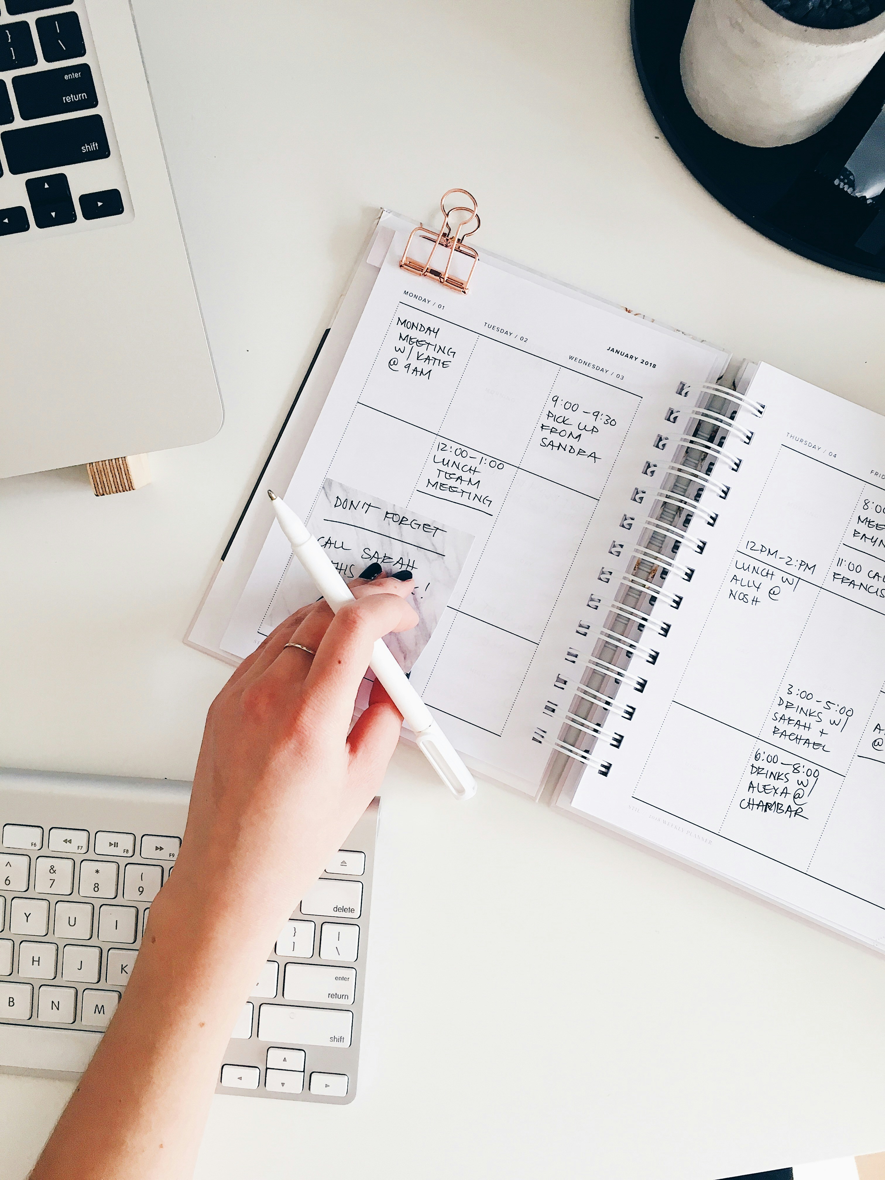 Hand writing in a planner at a clean white desk